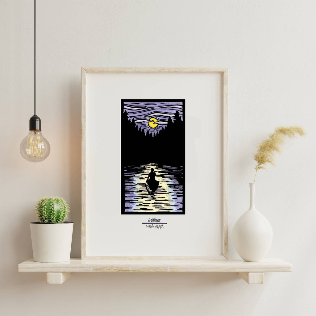 On a shelf sits the "Solitude Canoe" 11"x14" giclee print, expertly framed and capturing a silhouetted figure peacefully canoeing across a moonlit lake under a purple sky. This Sarah Angst artwork is complemented by the presence of a cactus, vase, and hanging bulb, emanating an aura of serene tranquility.