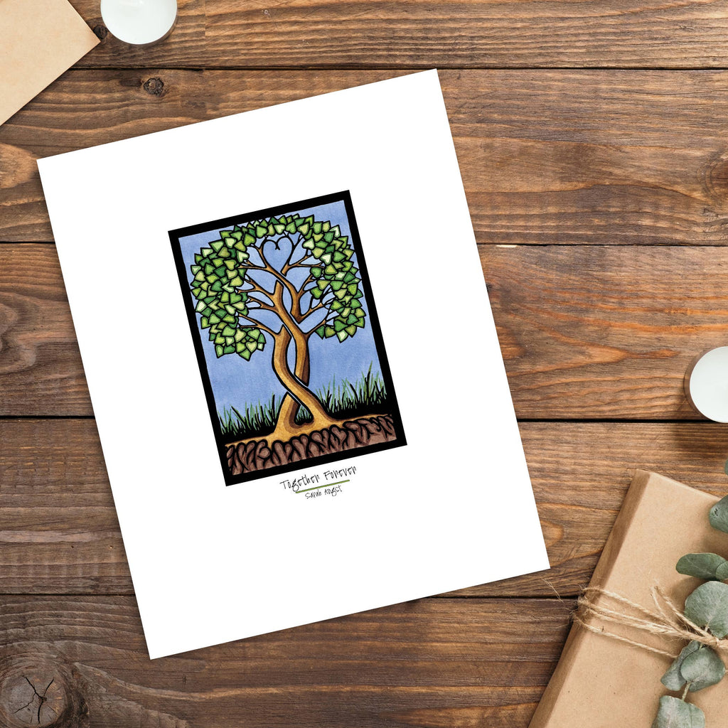 A card featuring a stunning Artwork: Together Forever Tree Giclee Art Print in 11"x14", depicting a tree with heart-shaped leaves on a wooden surface, beautifully arranged next to a wrapped gift and two candles. This Heart Tree Print is perfect for expressing love and gratitude, making it an ideal Valentine's Day gift.