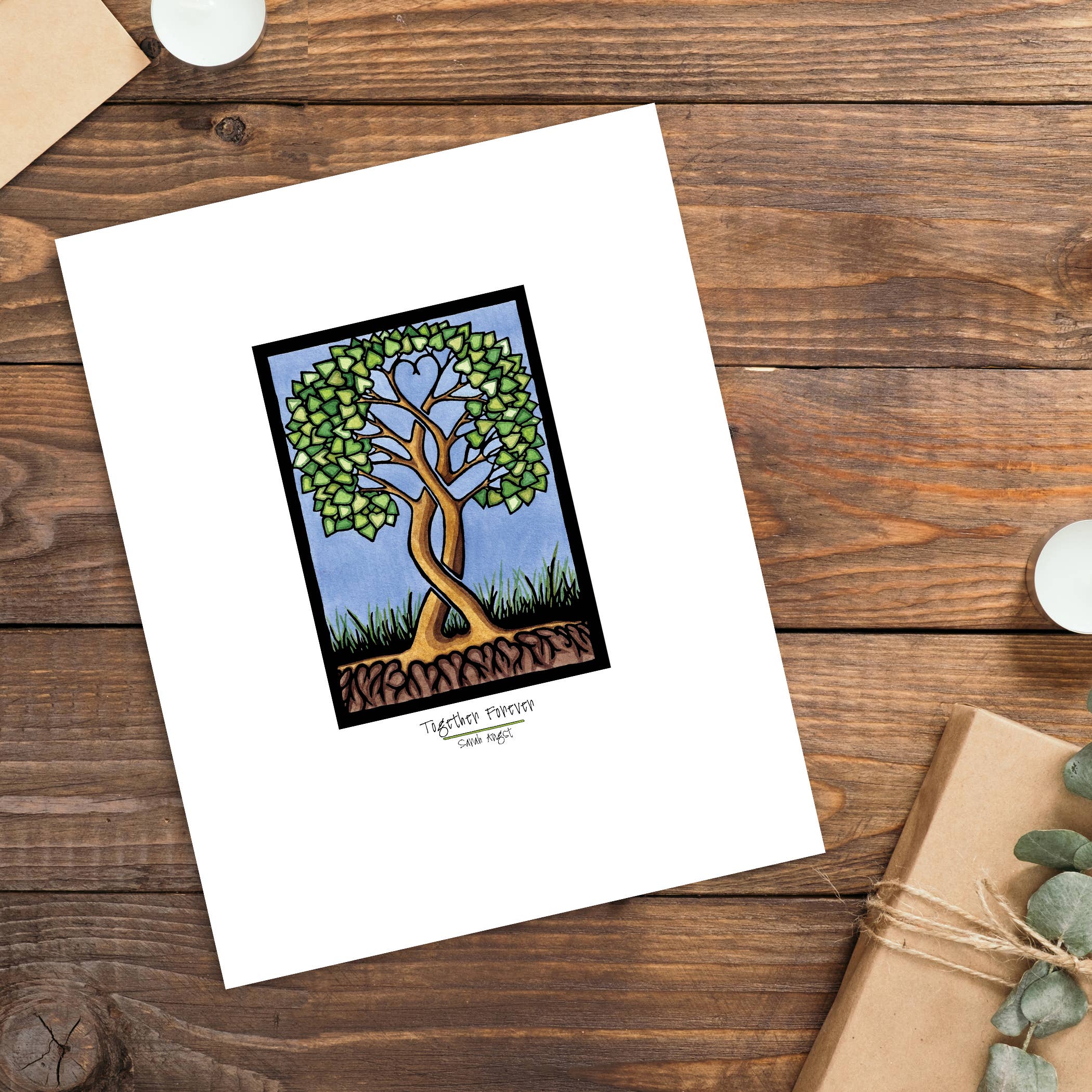 A card featuring a stunning Artwork: Together Forever Tree Giclee Art Print in 11"x14", depicting a tree with heart-shaped leaves on a wooden surface, beautifully arranged next to a wrapped gift and two candles. This Heart Tree Print is perfect for expressing love and gratitude, making it an ideal Valentine's Day gift.